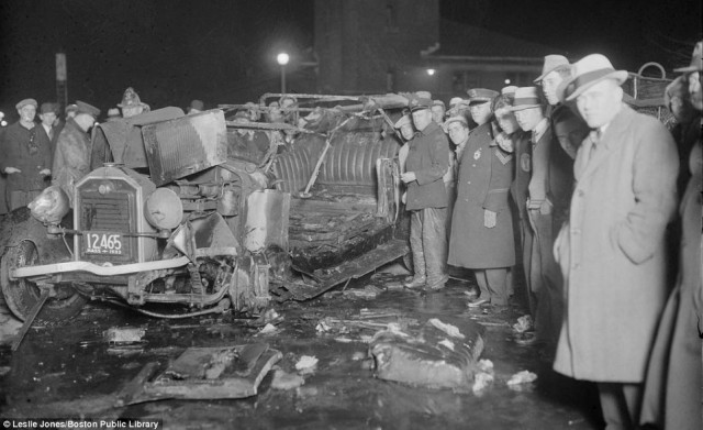 Crowds pose for photographer Leslie Jones alongside a mangled and burnt out wreck in Boston in 1933